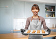 cooking, culinary and bakery concept - happy smiling female chef or baker in apron holding baking tray with oatmeal cookies over kitchen background