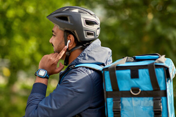 Wall Mural - food shipping, technology and people concept - happy smiling delivery man in bicycle helmet with thermal insulated bag and earphones listening to music on city street