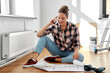 © Syda Productions - repair, people and real estate concept - woman with blueprint and pencil sitting on floor at home and calling on smartphone