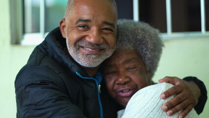 Wall Mural - A black adult son hugging senior mother posing for camera together