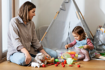 Sticker - family, leisure and people concept - happy mother and little baby daughter playing tea party with set of toy dishes at home