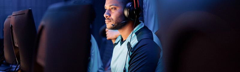 Wall Mural - Focused African professional gamer participating in online cyber games tournament while sitting at pc gaming club