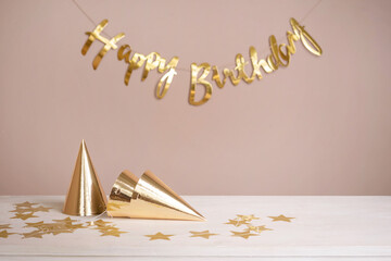 Wall Mural - Golden party caps and an inscription happy birthday on the table. Beige festive background with copy space.