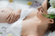 High angle view of pregnant woman touching blurred belly in bath with flowers and milk at home