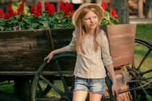 Dreamy Preteen Girl Leaning On Wheel Of Old Wooden Cart Used As Flower Bed Outdoors