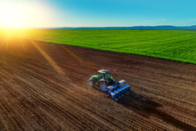 Farmer With Tractor Seeding Crops At Field