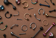 Stylish Piercing Jewelry On Brown Background, Flat Lay