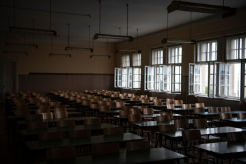 Empty old faculty or college School classroom with row of chairs, green desk tables and big white windows. Natural light.