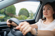 © DG PhotoStock - Happy Asian woman driving the electric vehicle - EV car smiling and showing her thumb up to the camera, happy and safety driving concept. Woman driving modern EV car and smiles to camera.