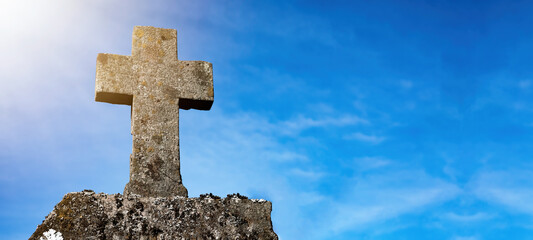 Wall Mural - Religious Background - Blue cloudy sky withold weathered stone cross, illuminated by the sun