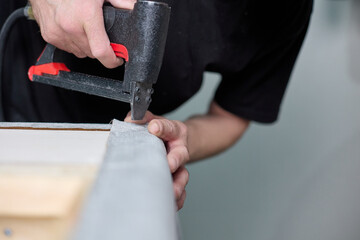 Production of upholstered cabinet furniture. Worker qualitatively fixes the fabric with a pneumatic stapler on the body in the factory shop. 