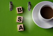 © Zhanna - BSA - acronym on wooden cubes against the background of a green folder and a cup of coffee