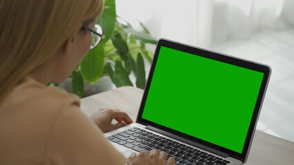 Over the shoulder shot of a business woman working in office interior on pc on desk, looking at green screen. Office person using laptop computer with laptop green screen.