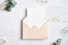 Pink Envelope With White Paper Card Inside And Eucalyptus Branches On Marble Table