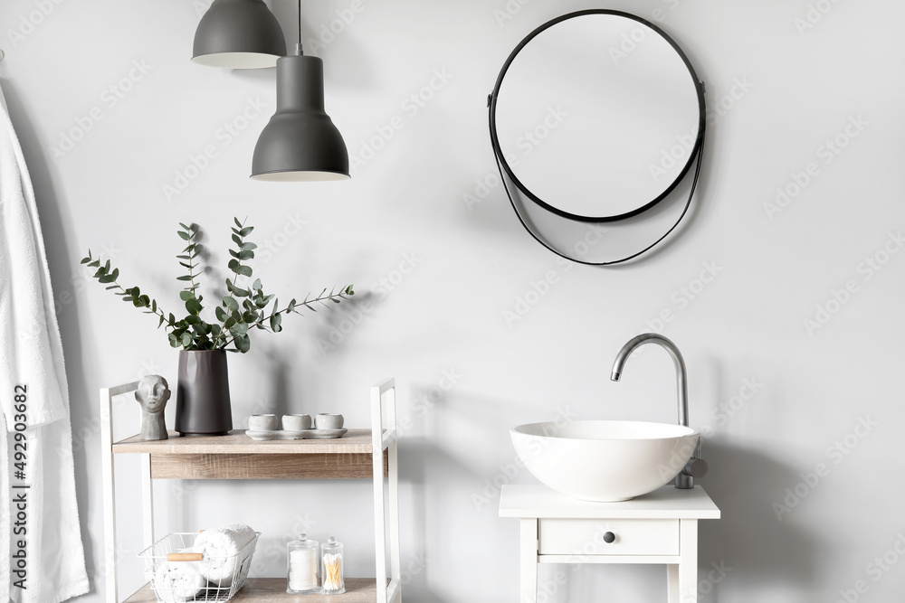 Interior of light bathroom with small table, sink and shelving unit