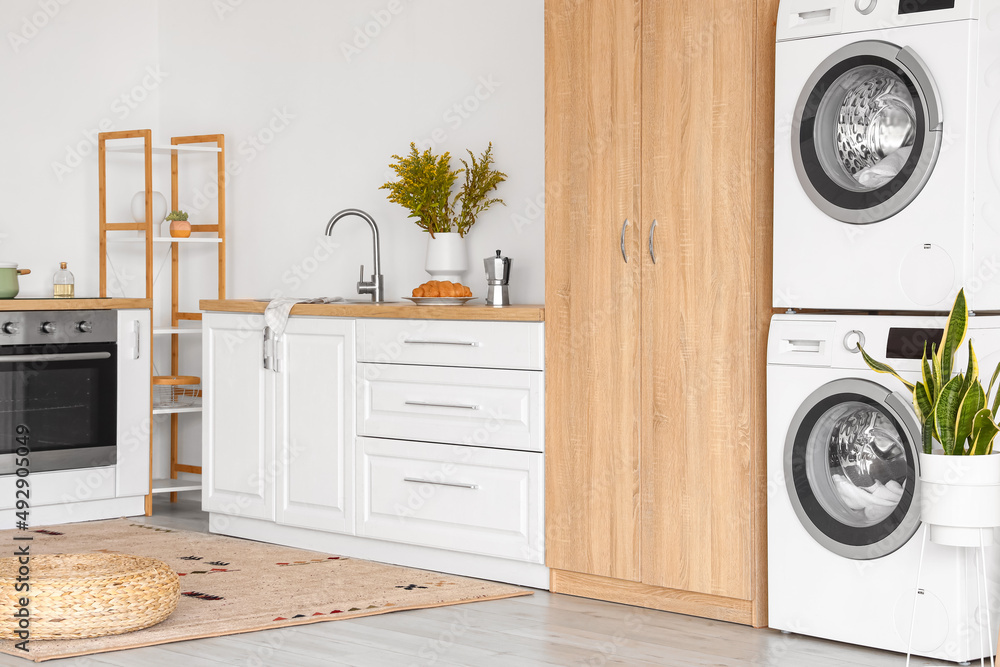 Interior of light kitchen with washing machines, white counters and cupboard