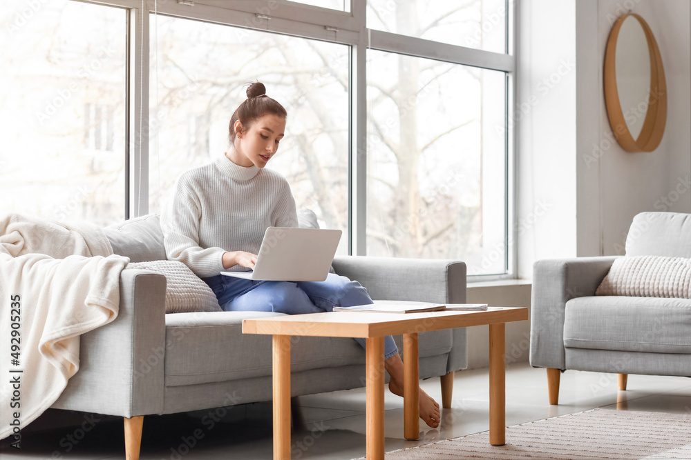 Beautiful young woman with laptop resting on couch at home