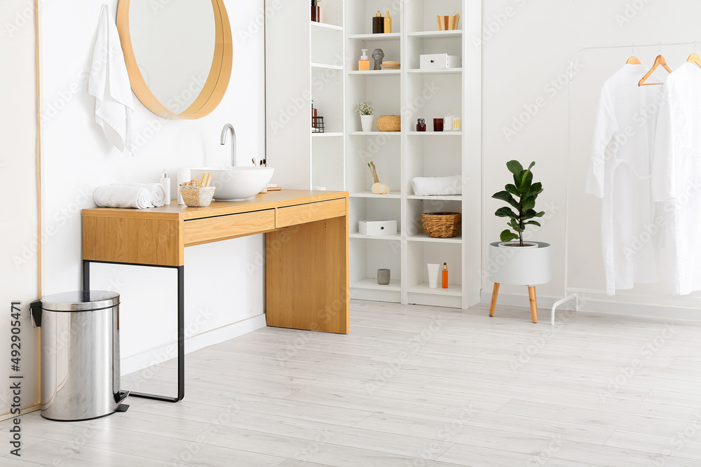 Stylish interior of bathroom with shelf units and table with different bath supplies