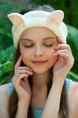 Poster - Beautiful little teenage girl with funny cat headband is smiling front of tropical leaves background. Portrait of cute little child enjoying skin care procedures