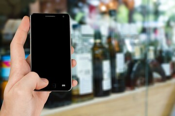 Sticker - Hand with blank smartphone screen on Wine shop with bottles background.  Buying and ordering alcoholic