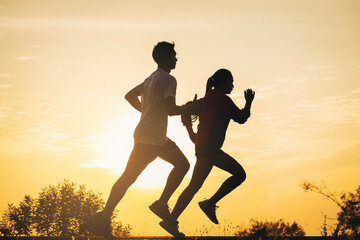 Wall Mural - Silhouette of young couple running together on road. Couple, fit runners fitness runners during outdoor workout with sunset background.