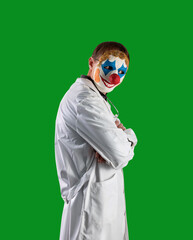 Wall Mural - Not an honest doctor in a clown mask on a green isolated background. With a medical stethoscope. Deception in treatment. Halloween.