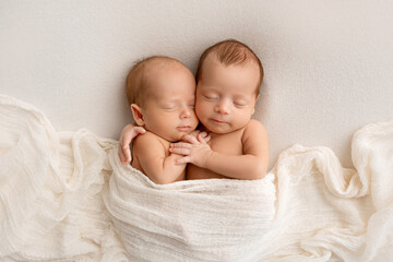 tiny newborn twins boys in white cocoons on a white background. a newborn twin sleeps next to his br