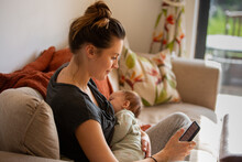 Mum Breastfeeding Her Newborn Baby And Using A Smartphone