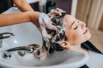 Wall Mural - Professional hairdresser washing hair of a beautiful young  woman in hair salon.