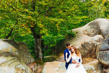 Wall Mural - the groom embraces the bride from the back side among the rocks