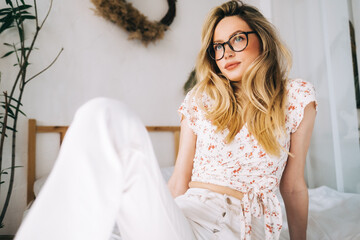 Wall Mural - Portrait of attractive young happy caucasian woman in glasses, sitting in cozy bedroom.