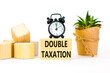 Double taxation symbol. Concept words Double taxation on wooden blocks on a beautiful white table white background. Black alarm clock. Business tax and double taxation concept, copy space.
