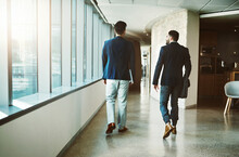 Success Doesnt Happen Until People Get Moving. Rearview Shot Of Two Young Businessmen Walking Down A Corridor Of A Modern Office.