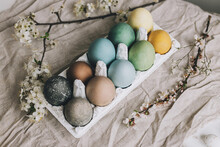 Stylish Easter Eggs And Cherry Blossoms On Rustic Linen Cloth. Happy Easter!  Natural Dyed Colorful Pastel Eggs In Tray And Spring Flowers On Rustic Table. Countryside Still Life