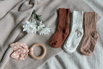 Layout of children's socks (newborns) among children's things: a beige plaid, a rattle-teether, flowers - chrysanthemums. 