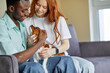 © Roman - young couple of different ethnicity sit on sofa playing loving pet dog, at home, nice family in casual clothes have fun, spend time together at weekends, holidays. indoors. friendship, love