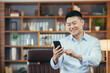 © Liubomir - Close-up portrait of Asian man working in classic home office, Businessman using phone looking at smartphone screen and smiling