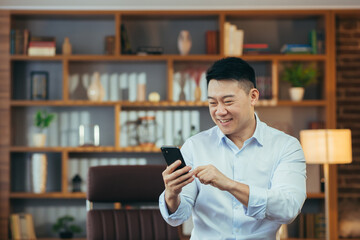 Close-up portrait of Asian man working in classic home office, Businessman using phone looking at smartphone screen and smiling