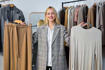 female blogger or stylist standing in front of camera showing clothes recording shopping video or fashion look tops, internet e-commerce concept. woman making choice, racks with outfits in background