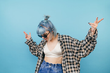 Wall Mural - Hipster girl with bright looks in summer clothes and sunglasses dancing on a blue background.