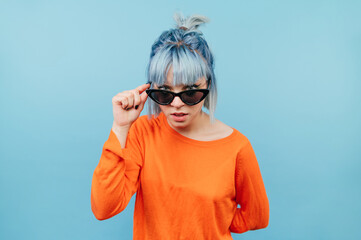 funny hipster girl with colored hair in sunglasses looks intently at the camera with a serious face.