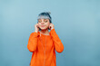 © bodnarphoto - Cute teen girl with blue hair and colored clothes listens to music in headphones with closed eyes on a blue background.