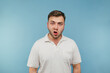 Surprised man with bristles on a blue background looks at the camera with a shocked face wearing a white T-shirt.