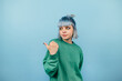 © bodnarphoto - Beautiful girl with blue hair and a serious face stands on a blue background and looks and points to the side on copy space