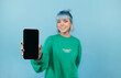 © bodnarphoto - Positive hipster girl with blue hair and with a smile on her face shows to the camera a smartphone with a black blank screen on a blue background