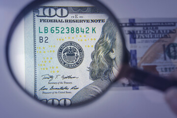 Magnifying glass on the background of a 100 dollars close-up. Concept on the theme of checking money for authenticity.