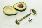 Fototapeta Mapy - Green ripe avocado with jade scraper gouache with facial serum on a light background.