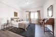 © Toyakisfoto.photos - Bedroom with king size bed with drawers and upholstered fabric headboard, vintage wooden desk and window with curtains and gray rug