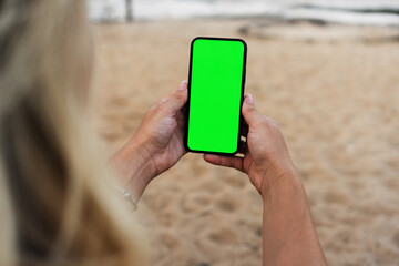 Girl on the beach holding a smartphone with Green screen. Chroma Key