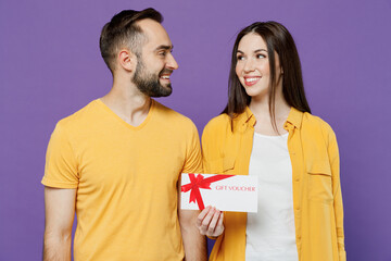 Wall Mural - Young happy fun couple two friends family man woman together in yellow casual clothes hold gift certificate coupon voucher card for store look to each other isolated on plain violet background studio.